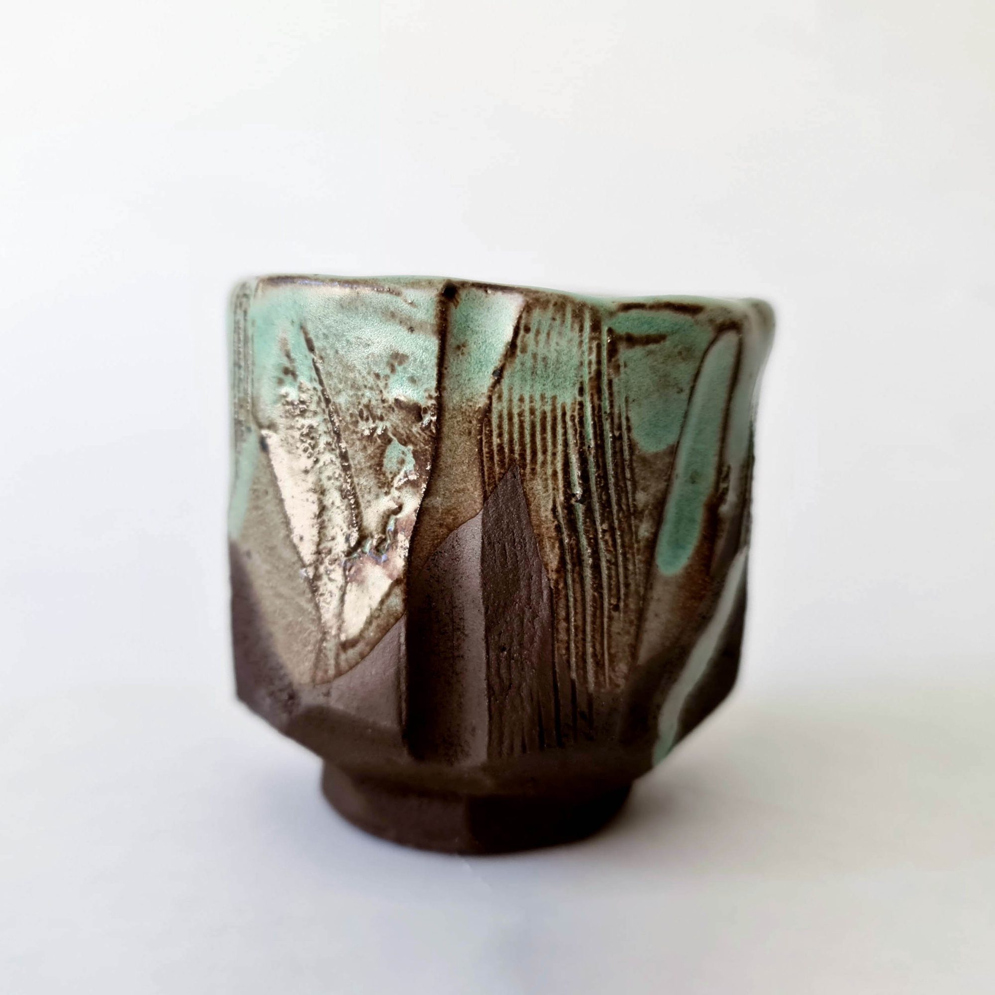 cup-kurinuki-turquoise-glaze Three hand-carved kurinuki cups in raw red clay, shown in natural light.