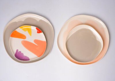 Two sets of layered porcelain plates — one with multicolored brushstrokes, the other in soft neutral tones.