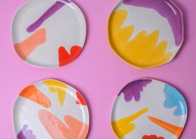 Four colorful porcelain plates with abstract brushstrokes on a pink background.