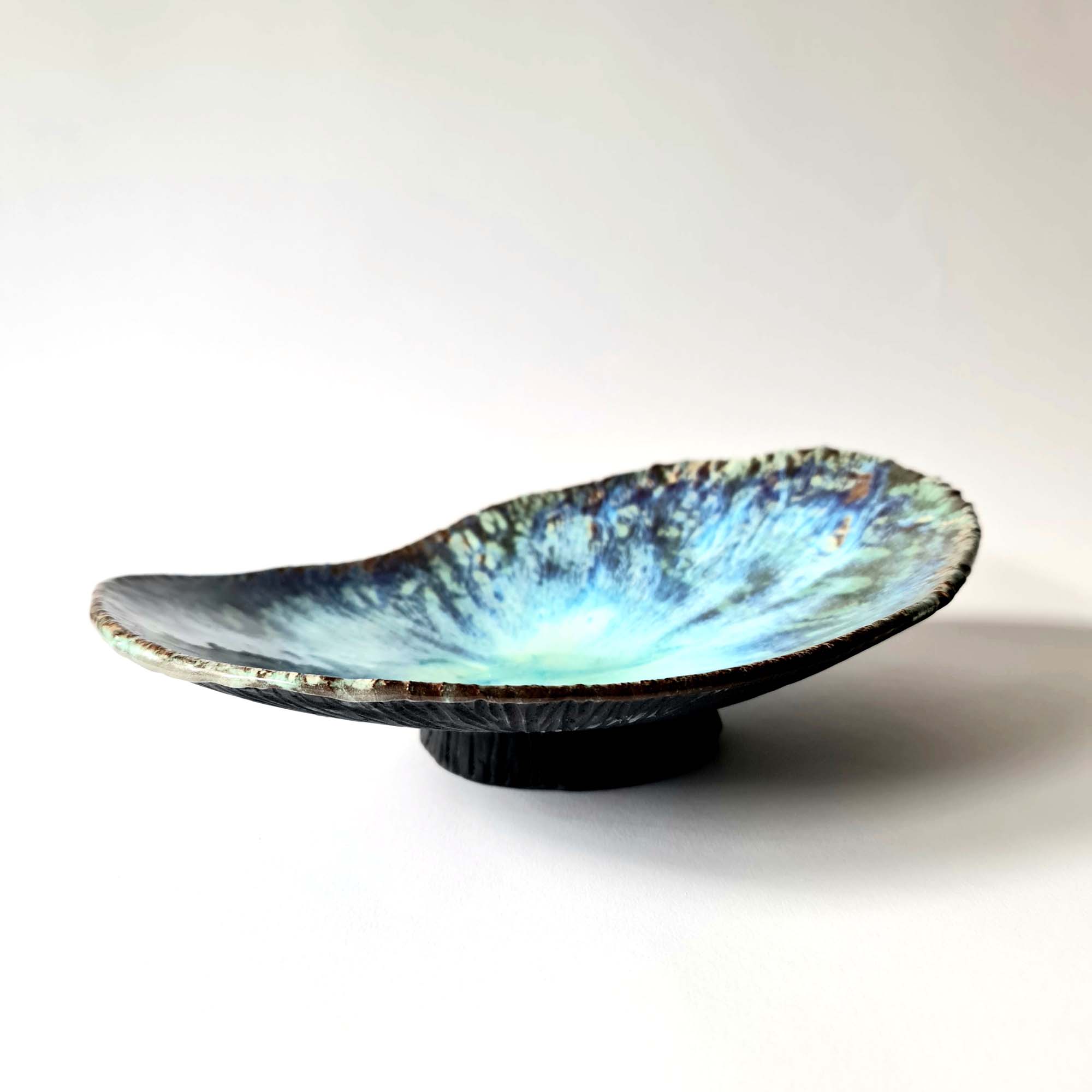 Sculptural bowl in black porcelain with layered blue floating glazes and textured exterior