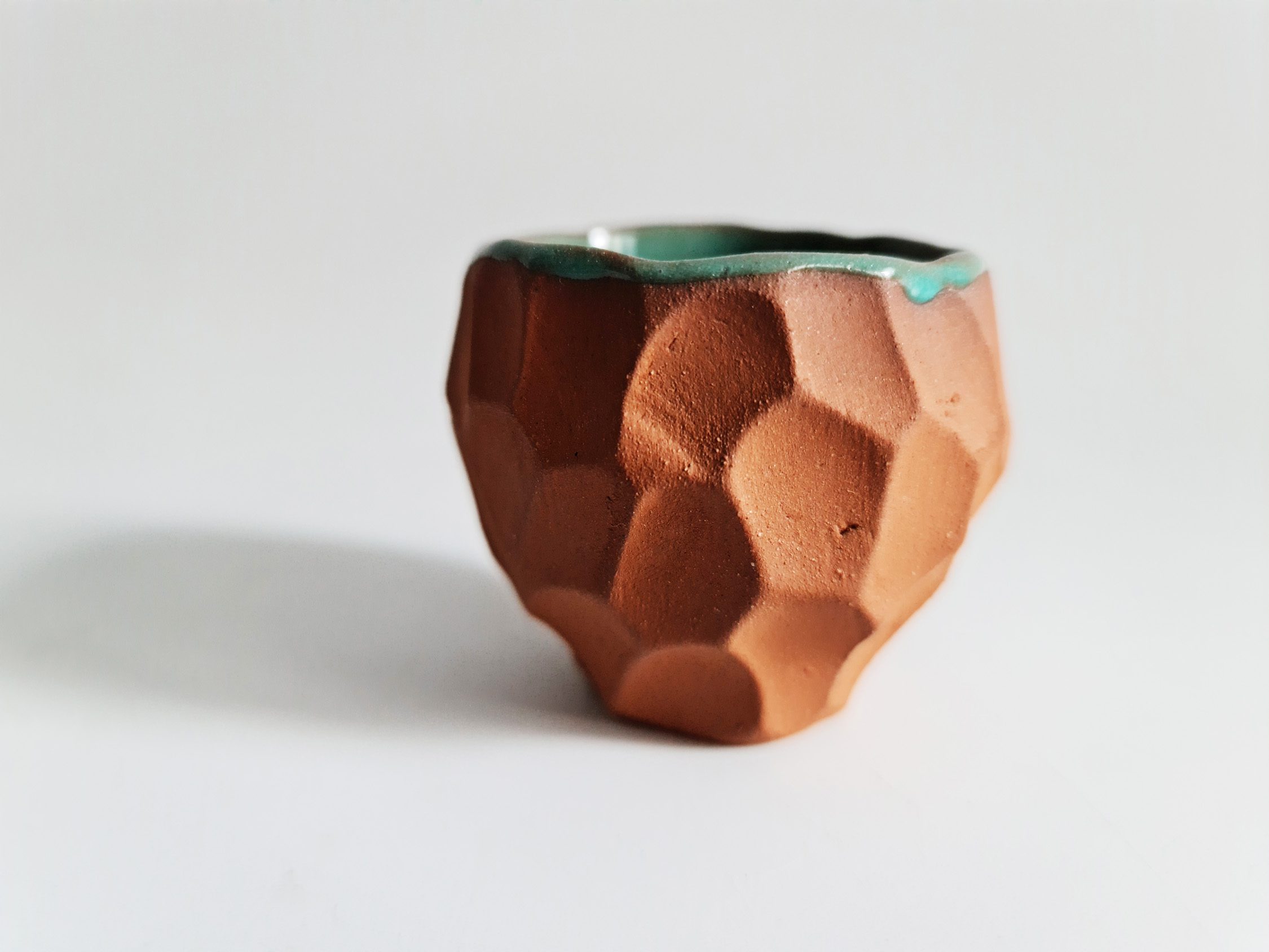 painted ruins cup Faceted terracotta cup with a green glazed interior on a white background.