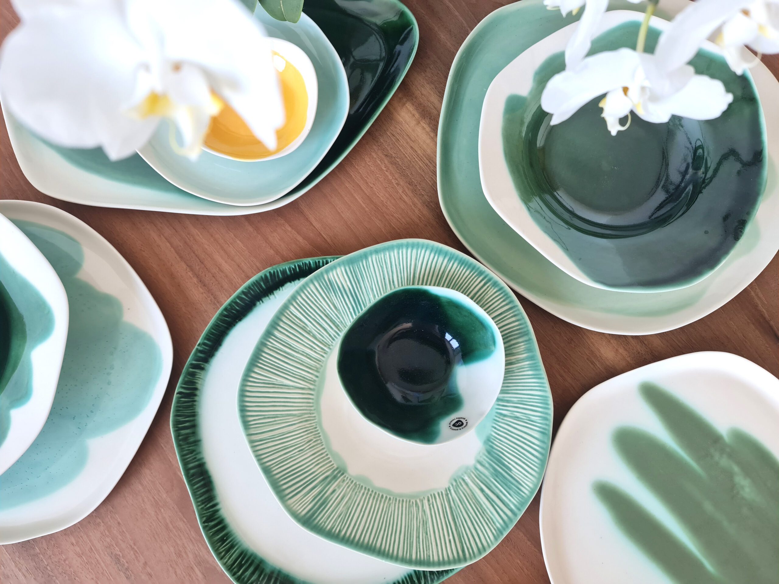 textured and color collection Top view of a spring-inspired table setting with handmade porcelain plates and bowls in soft and deep greens, featuring both smooth and textured designs.