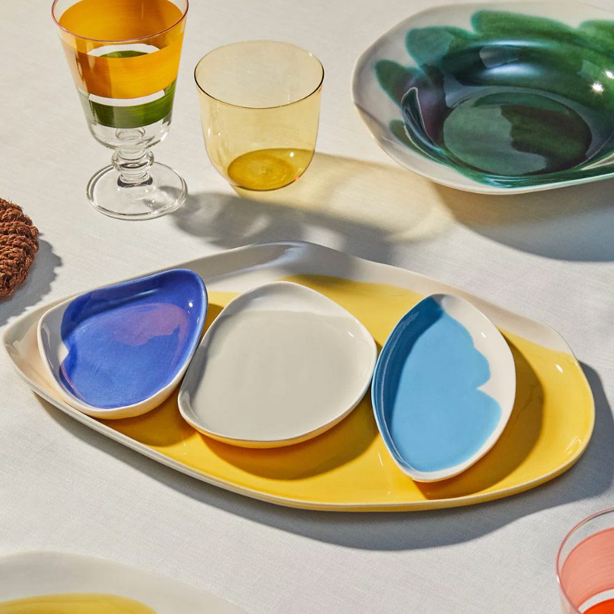 tray set with plates Colorful ceramic tray set with three small dishes in blue, white, and sky blue on a yellow base, styled on a dining table.